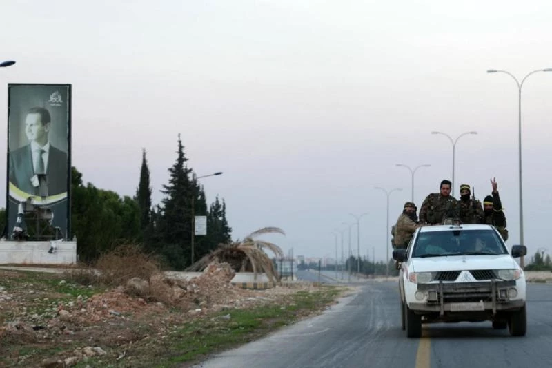 Suriye’nin kuzeybatısında yeni ele geçirilen Han el-Asel bölgesinde, Halep-Şam karayolu üzerinde Suriye Devlet Başkanı Beşşar Esad'ın bir posterinin yanından geçen muhalif grupların üyeleri, 29 Kasım 2024